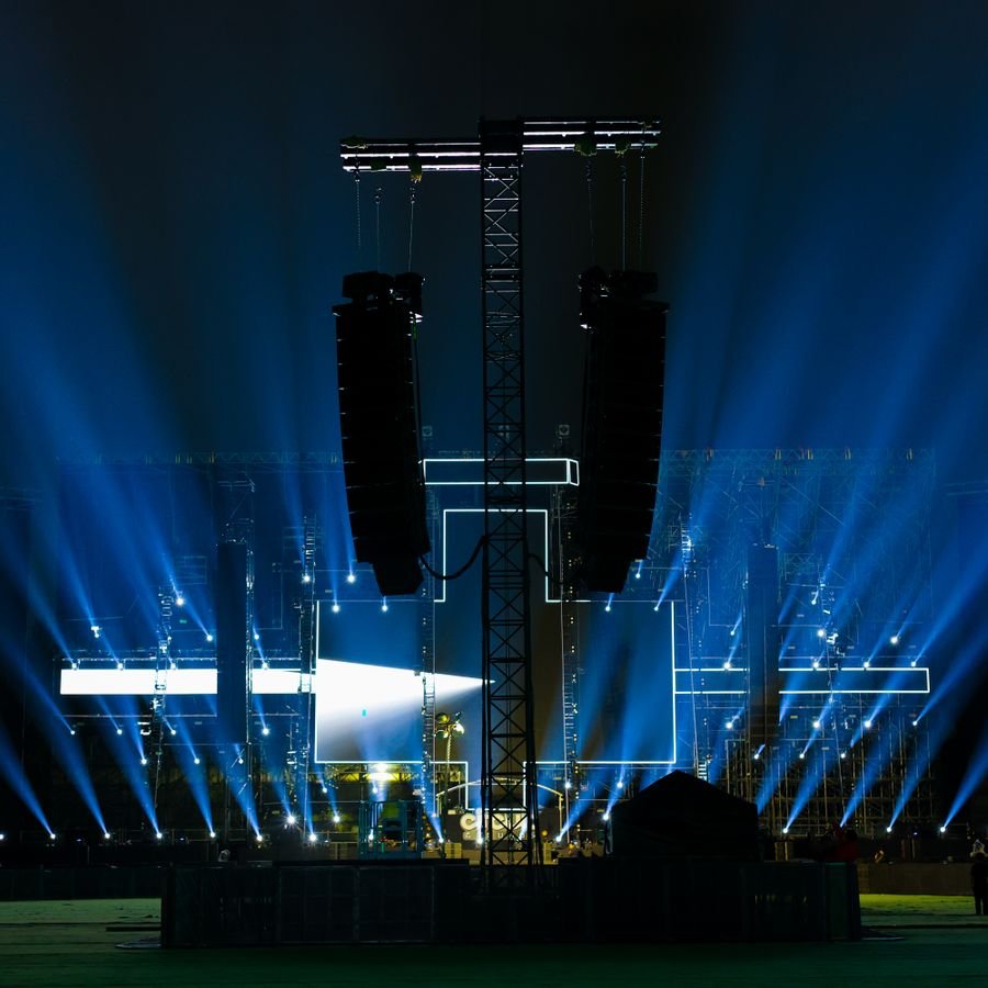 Twin line arrays flown above a concert stage with blue light beams